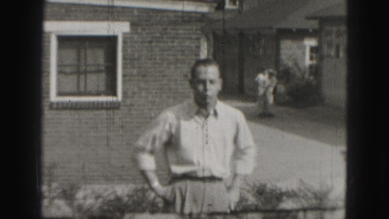 In the Harrisburg 1946 home-movie frame, a man stands on a lawn before a brick house with another adult and small dog behind him.