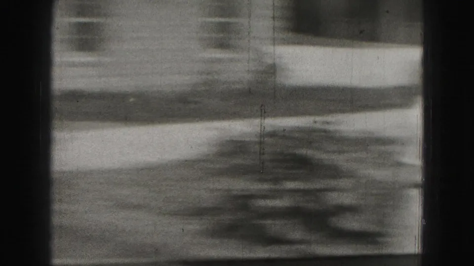 A soft, motion-blurred 8mm frame shows ground or lawn area with dark shadows and visible film gate borders.
