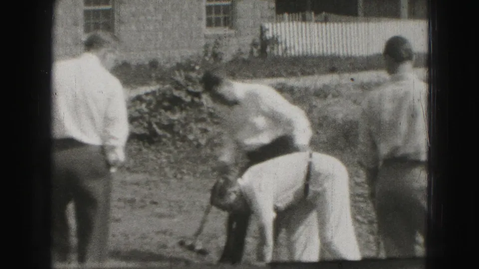 1946 Harrisburg home-movie frame showing men in dress shirts and trousers gathered around a backyard croquet shot.