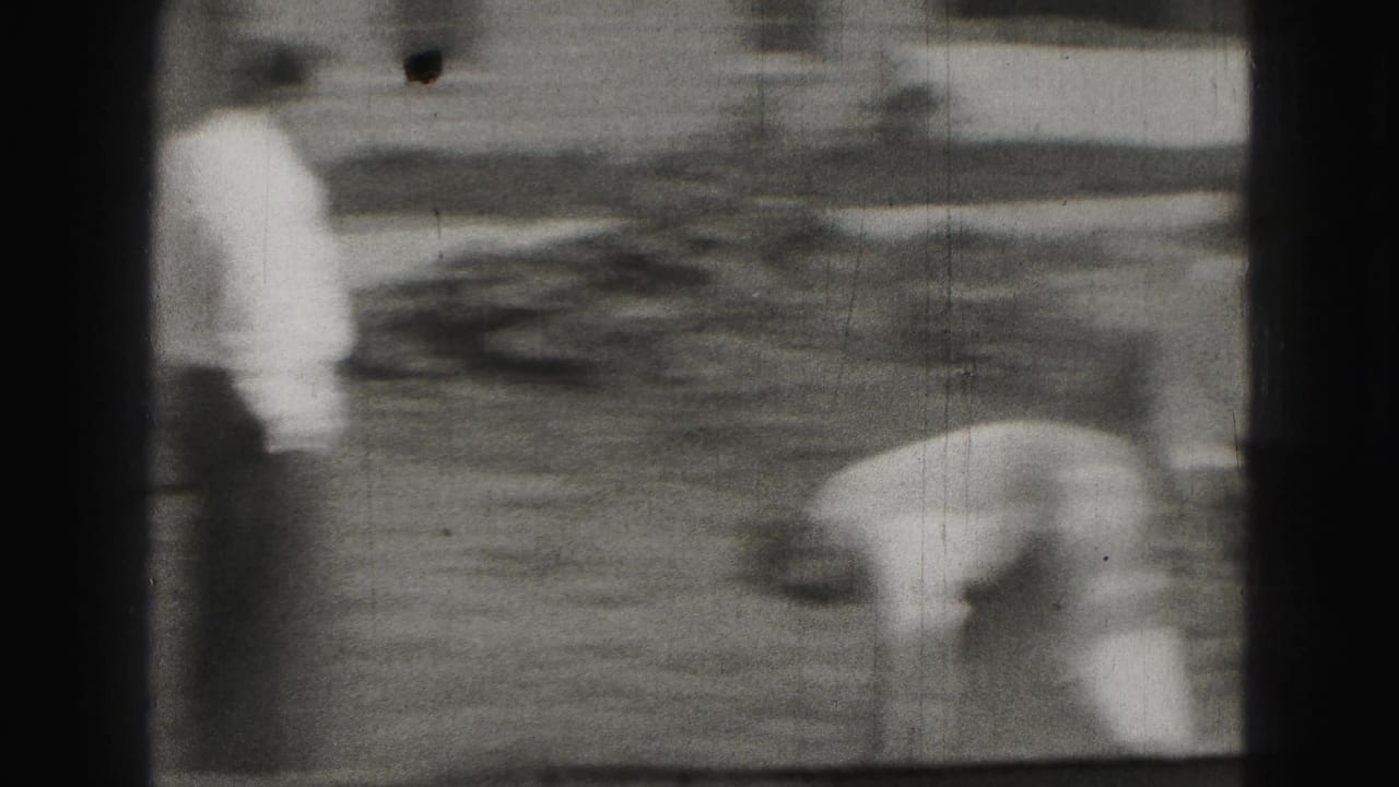 A man bends over the lawn while another stands nearby in a blurry croquet scene.