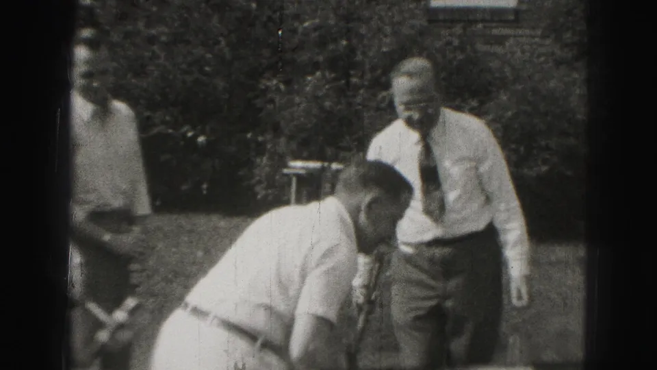 1940s Harrisburg backyard frame with men in dress shirts and ties watching a croquet player bend near the grass.