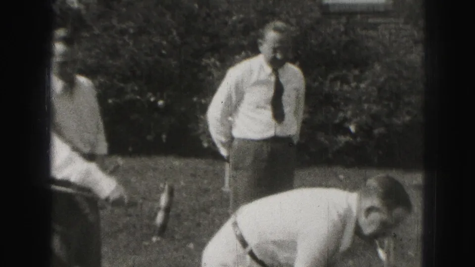 Harrisburg 1946 home-movie frame showing a tied man standing near a bent croquet player on a backyard lawn.