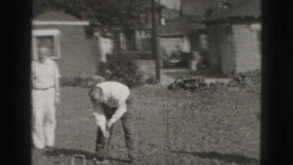 Two adult men appear in a Harrisburg yard, with one leaning over a croquet mallet near a modest house in 1946 footage.