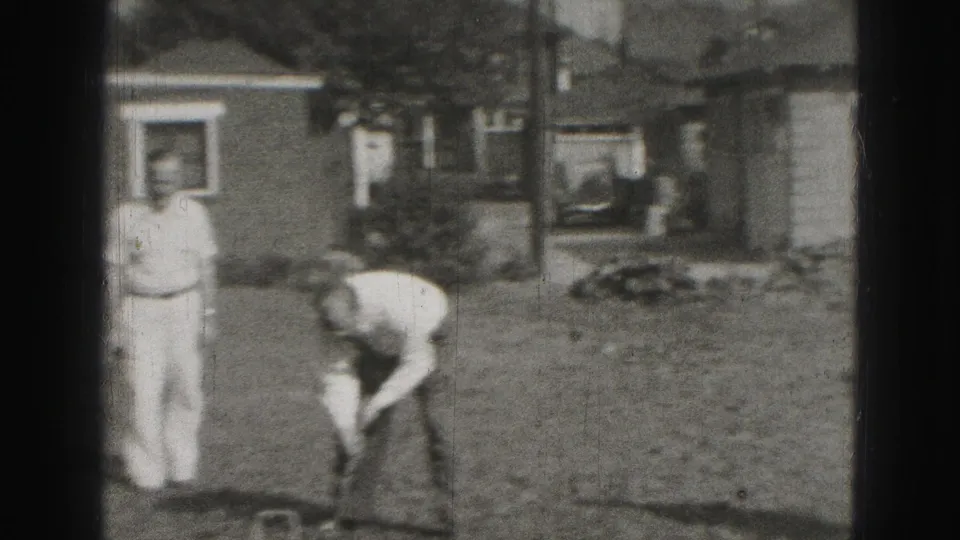 A 1946 Harrisburg home-movie frame shows a standing man watching another bend over a croquet play on a residential lawn.
