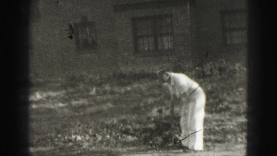 Adult man bends over in the Harrisburg yard, likely lining up or retrieving a croquet ball, with a house exterior behind him.