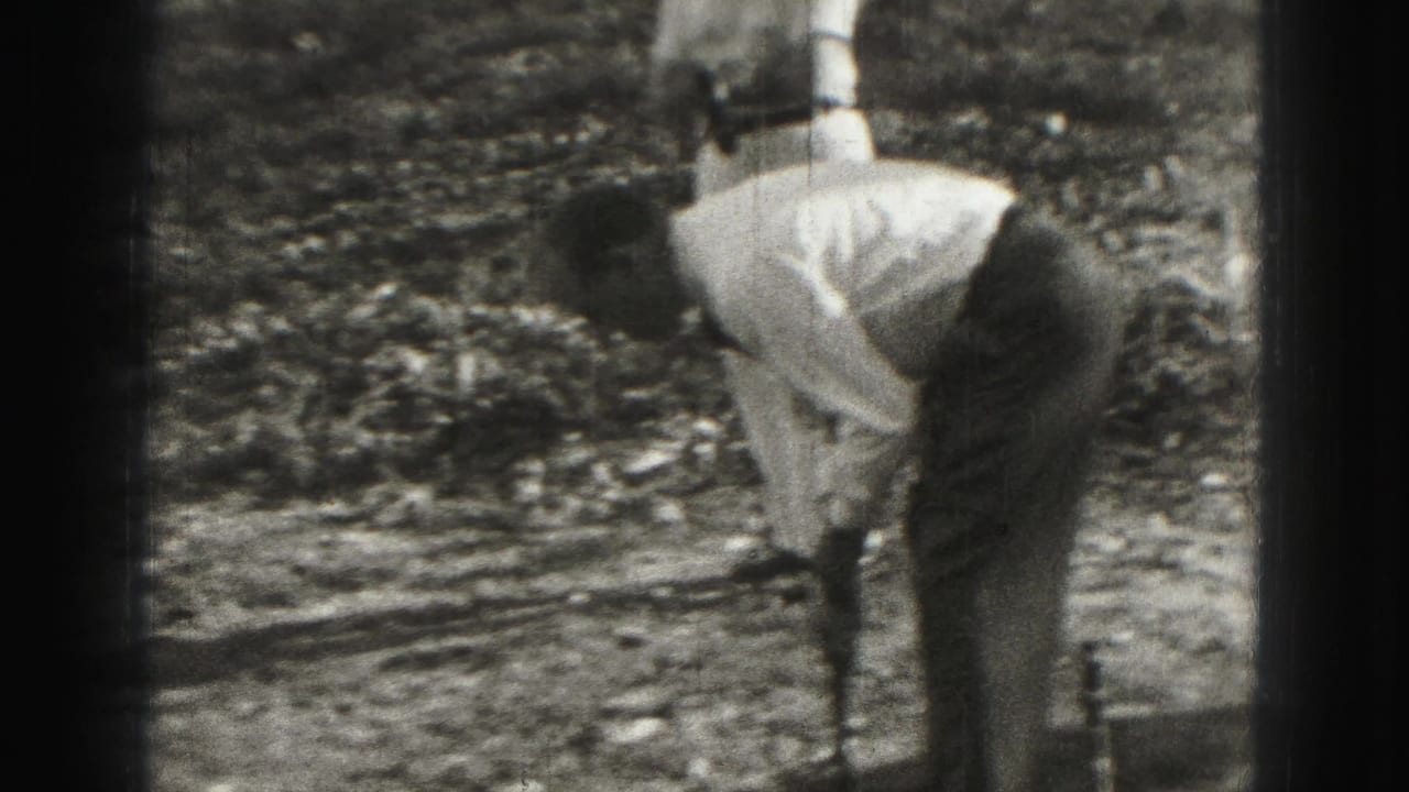 Man bends over a croquet mallet on a sunny yard while another person stands behind him.