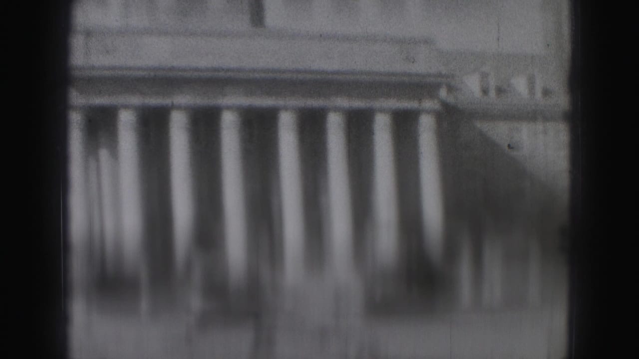 Out-of-focus black-and-white view of a building with repeated columns and dark borders.