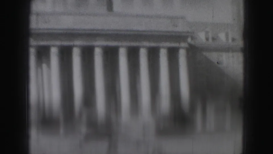 Blurred 8mm frame from the Harrisburg home movie showing repeated vertical columns on a building, with strong gate shadowing at the sides.
