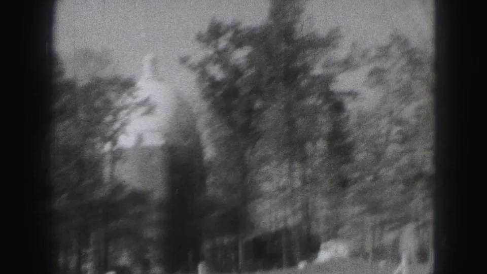 Black-and-white 8mm view of tree-lined grounds in Harrisburg with a building partly hidden in the background.