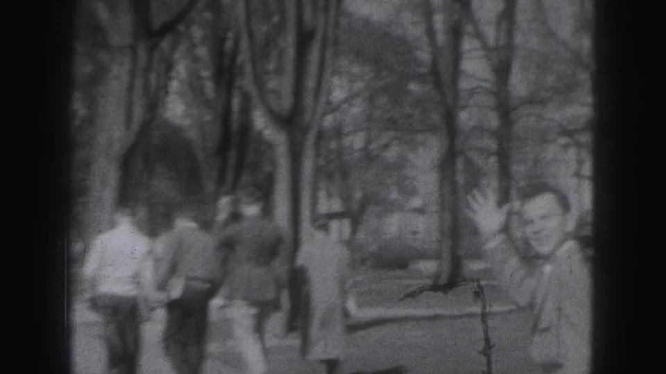 Black-and-white 1946 Harrisburg home-movie frame with suited adults walking through a tree-lined outdoor setting.