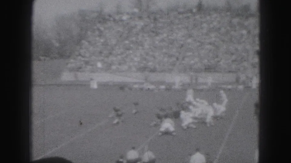 Soft 8mm frame from a 1946 Harrisburg football game showing players down on the grass as others approach the play.