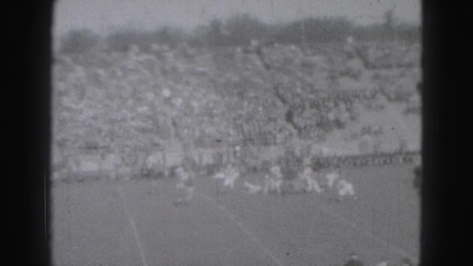 Distant 1946 Harrisburg football action appears near the sideline, with spectators filling the bleachers behind the field.