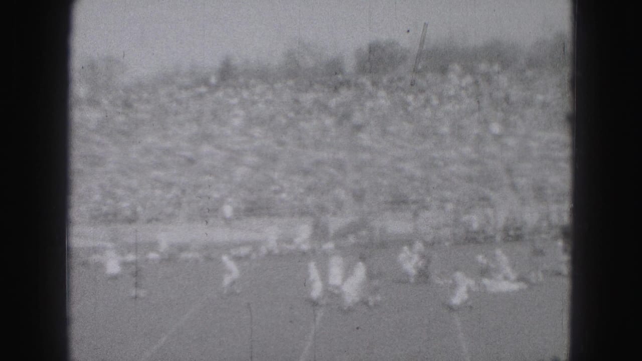 1946 Harrisburg home-movie view of distant football players on the field with crowded stands in the background.