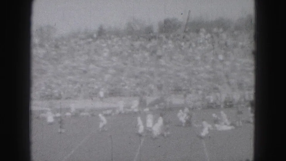 1946 Harrisburg home-movie view of distant football players on the field with crowded stands in the background.