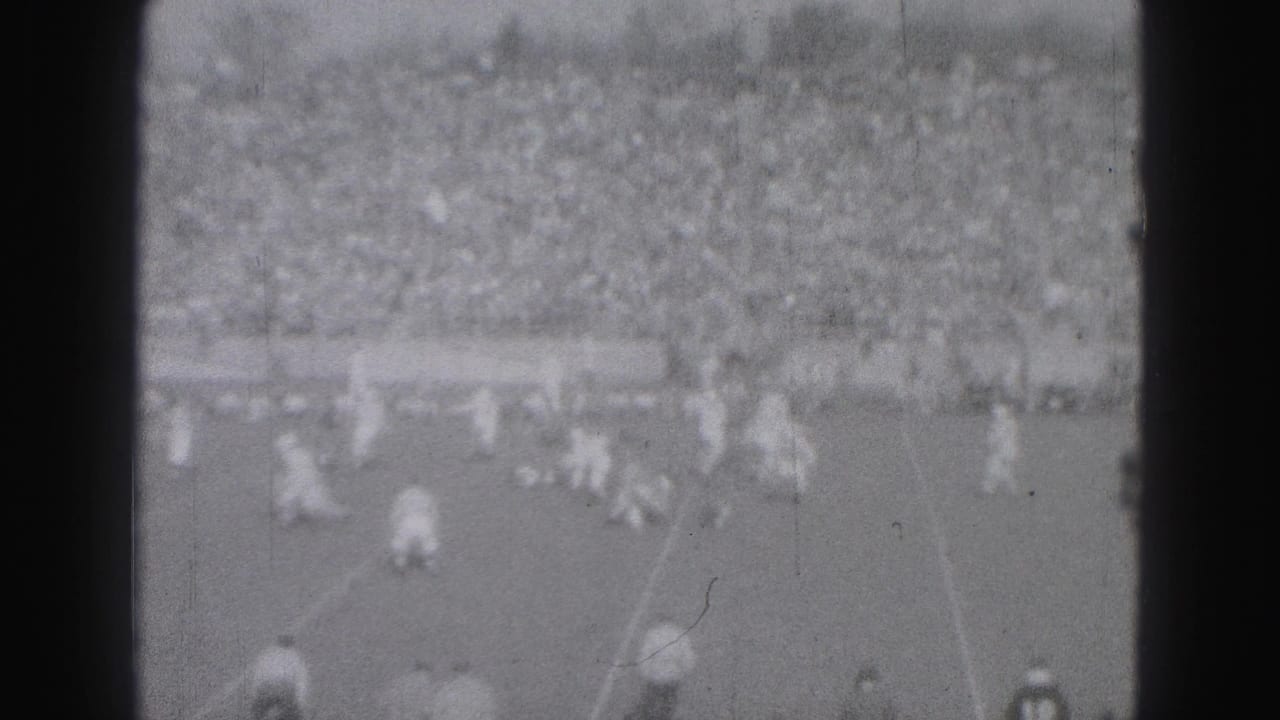 1946 Harrisburg home-movie frame showing distant field play before a packed stadium crowd.