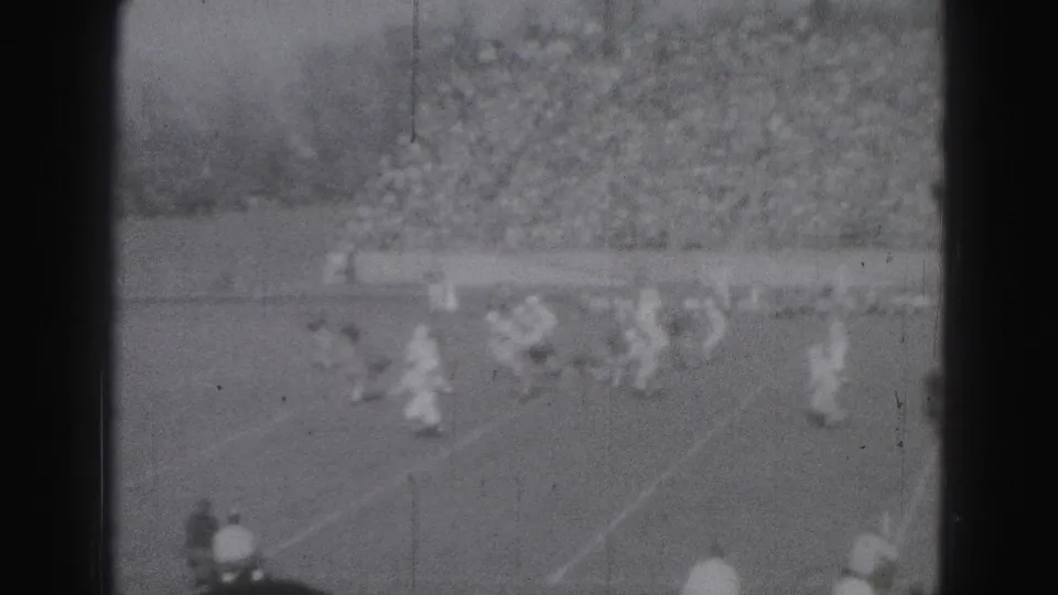 Mid-century 8mm frame of clustered field action at a crowded Harrisburg sports ground.