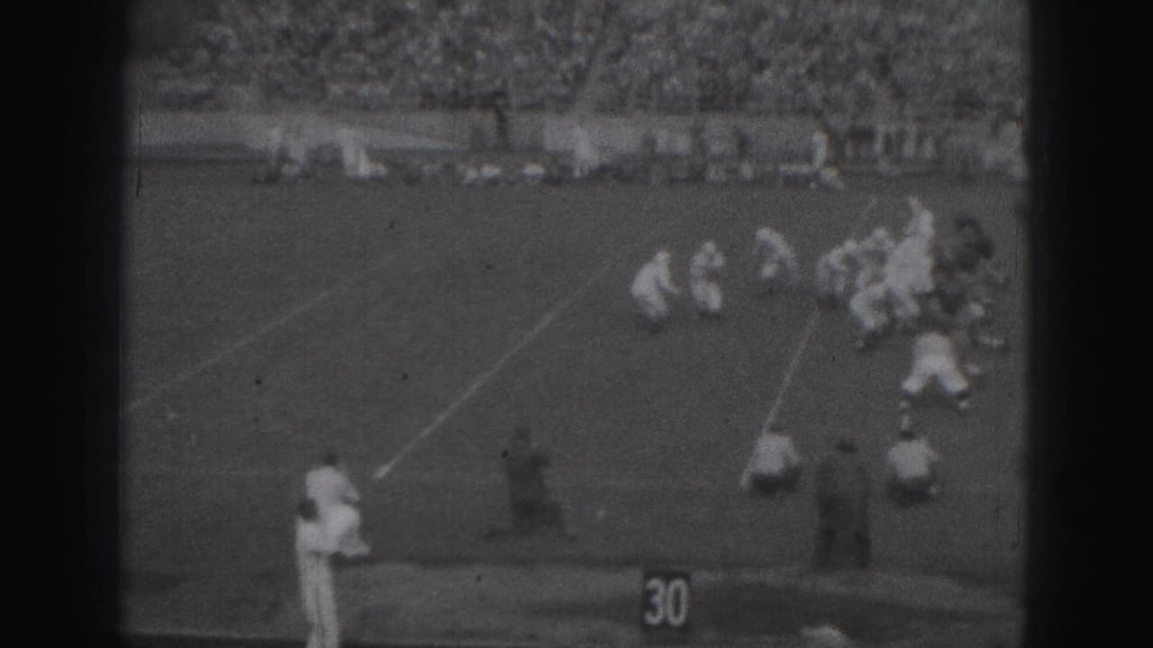 1946 Harrisburg football game footage showing players gathered near the 30-yard marker, with sideline figures and a packed stand behind them.