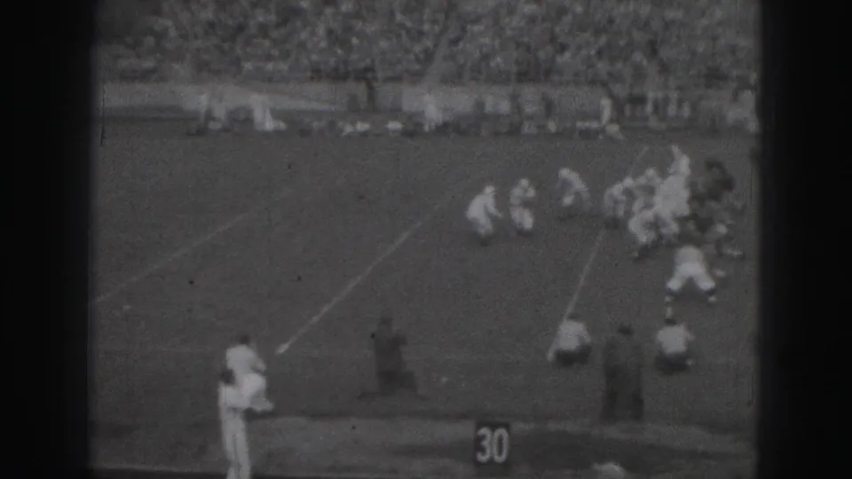 1946 Harrisburg football game footage showing players gathered near the 30-yard marker, with sideline figures and a packed stand behind them.