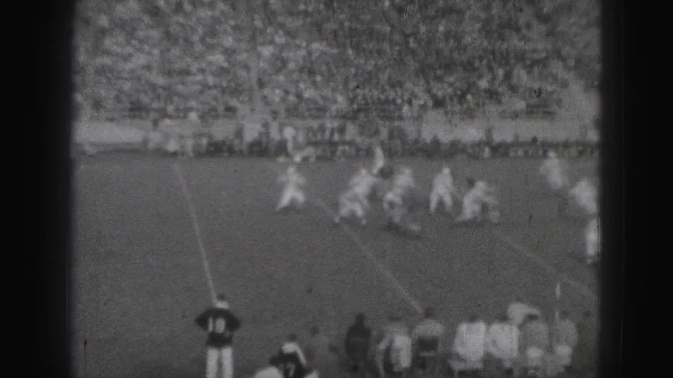 The football action continues on a Harrisburg field, with players moving through the play, spectators in the stands, and sideline figures at the edge of frame.