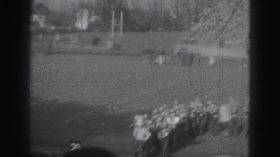 Distant 1946 Harrisburg stadium shot with football players near a line of band members and a large crowd behind them.