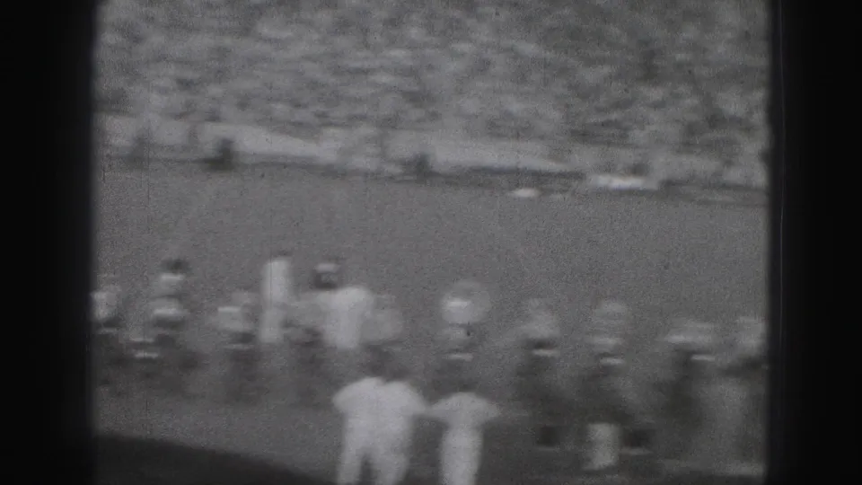 Soft 8mm view from the stands showing football players and sideline figures during the Harrisburg game.