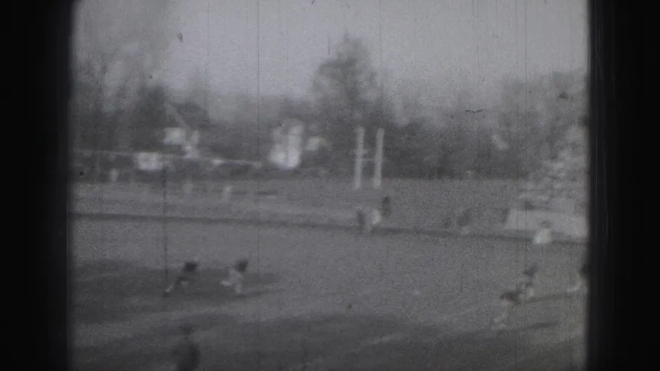 Harrisburg high school football players move across the field, with goalposts, trees, and spectators visible in the 1946 home-movie frame.
