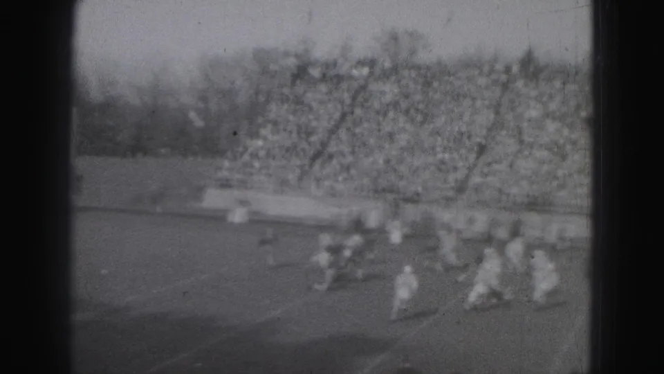 Players in light uniforms gather near the right side of the Harrisburg field, with a large crowd filling the bleachers behind them.