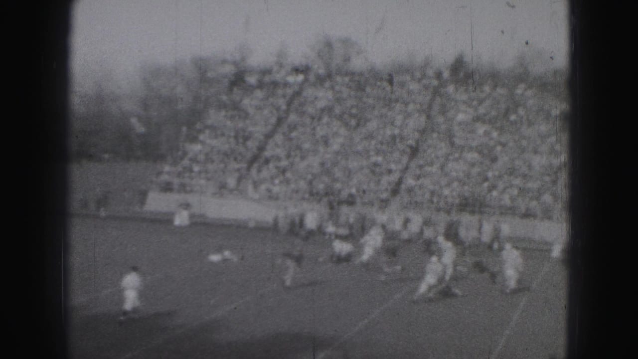Football players on a field with a packed grandstand in the background.