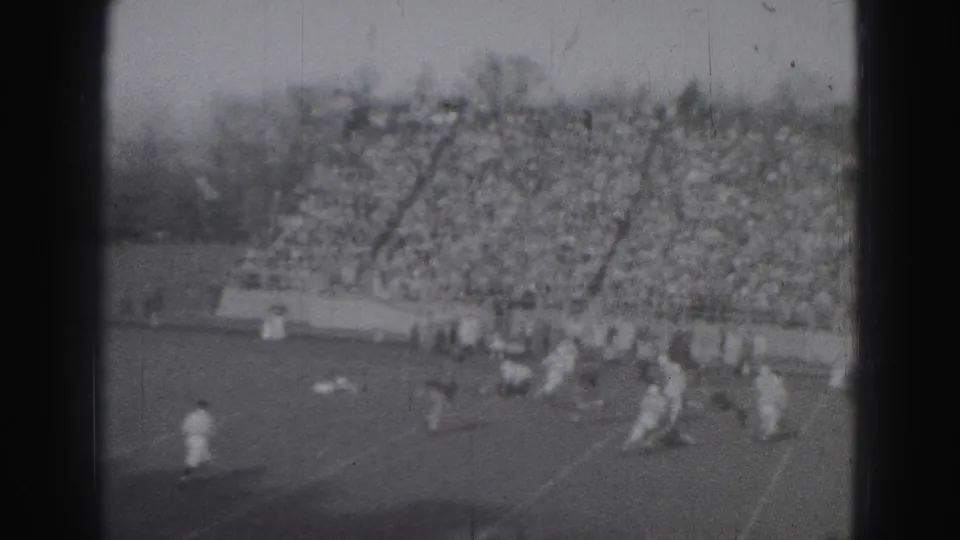 Distant 1946 Harrisburg football play seen from the stands, with players on the field and a large crowd behind them.