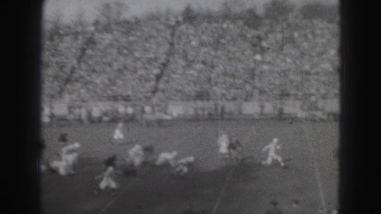 Players run and fall across the field with a large crowd in the background.