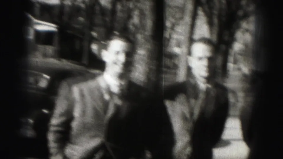 Soft-focused 1946 8mm frame of two suited men standing outdoors on a Harrisburg residential street.