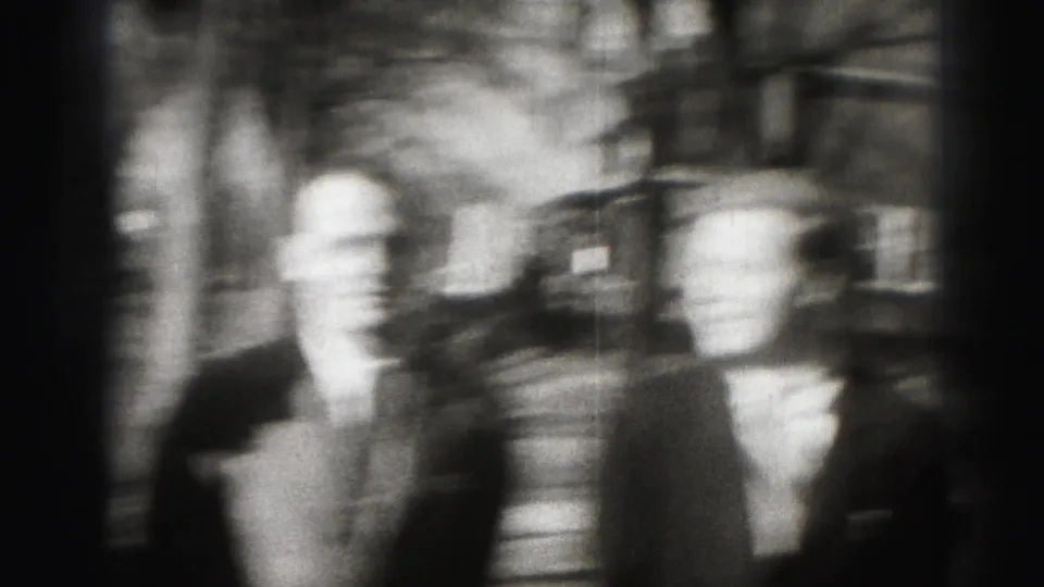 Motion-blurred black-and-white 8mm view of suited men on a Harrisburg street, likely during camera movement.