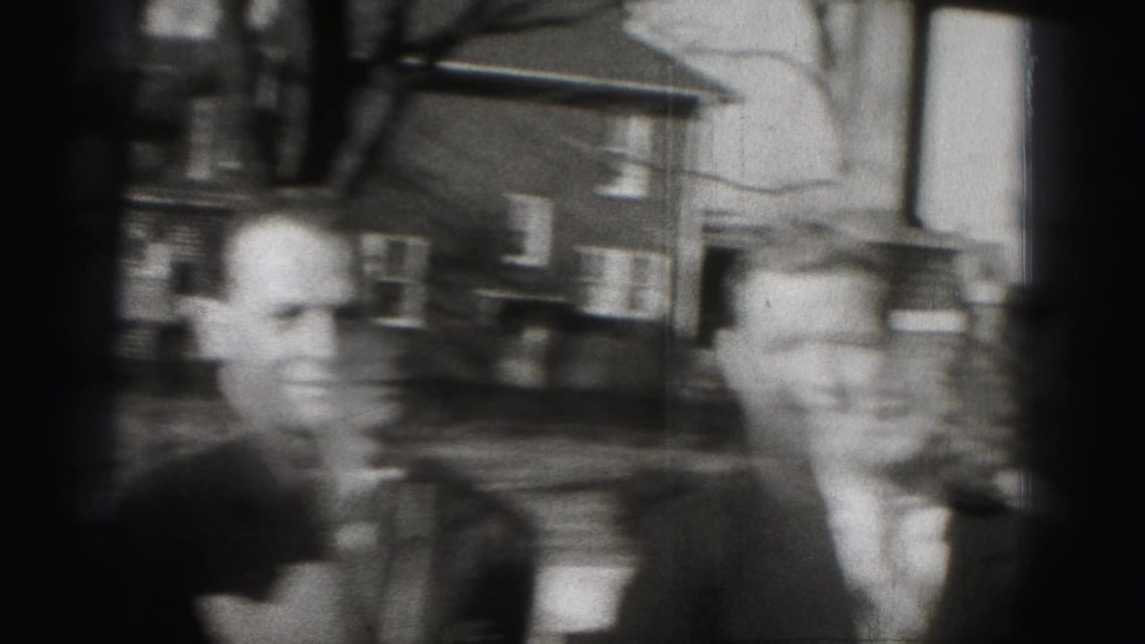 Two blurred men in suits stand or walk on a residential street.