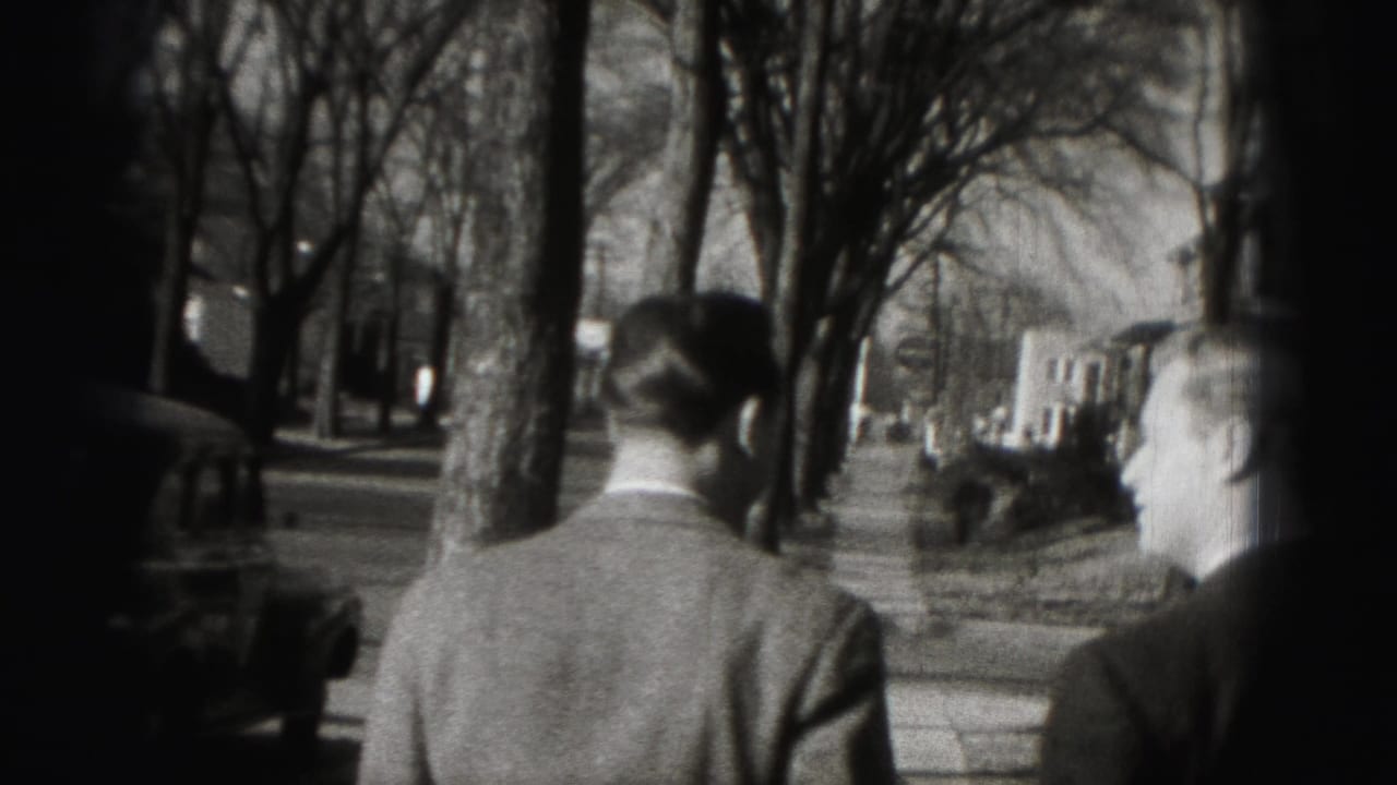 Two men in suits walk away from the camera on a tree-lined Harrisburg sidewalk in 1946 home-movie footage.