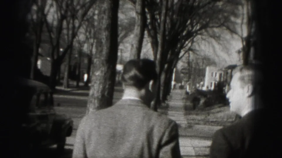 Two men in suits walk away from the camera on a tree-lined Harrisburg sidewalk in 1946 home-movie footage.