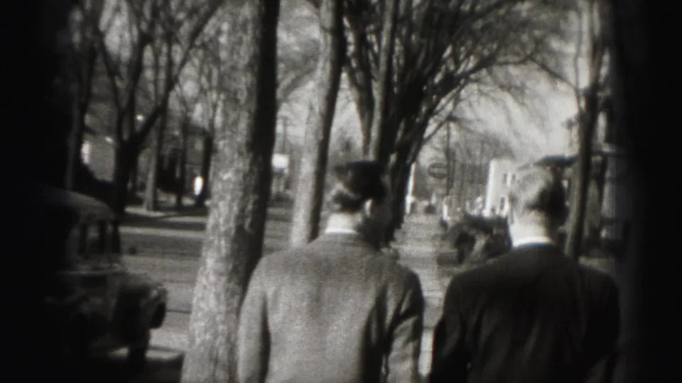 The two suited men continue down the Harrisburg sidewalk, seen from behind in black-and-white 8mm footage.