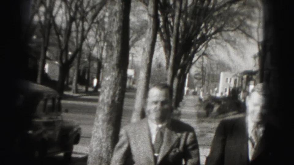 Two men in suits face the camera on the tree-lined Harrisburg street, with soft-focus 8mm texture visible.