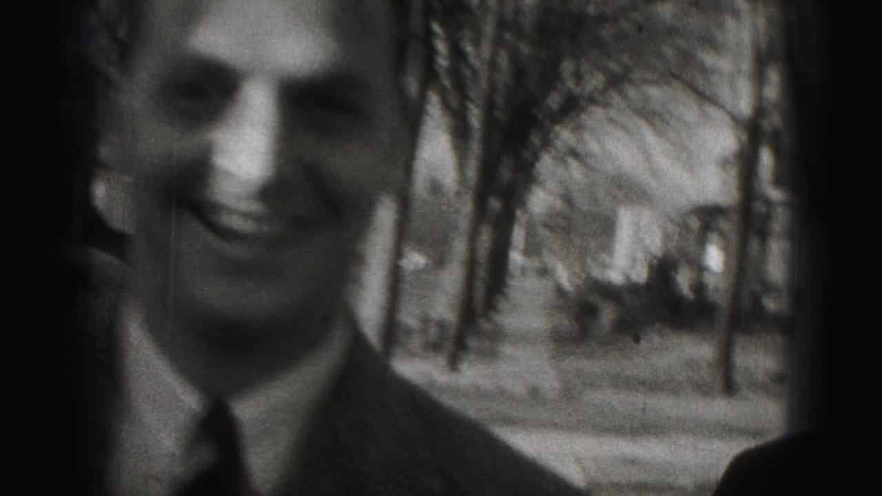 A smiling adult man in a suit appears close to the camera.