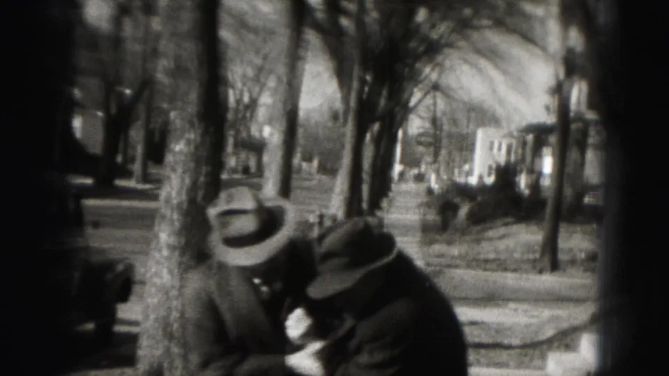 Two adult men in brimmed hats lean together on a residential Harrisburg street in 1946 footage.