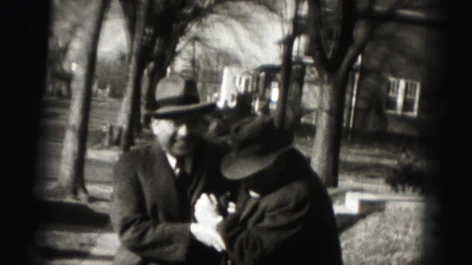 Two hatted adult men look down together on a tree-lined Harrisburg street in 1946 home-movie footage.