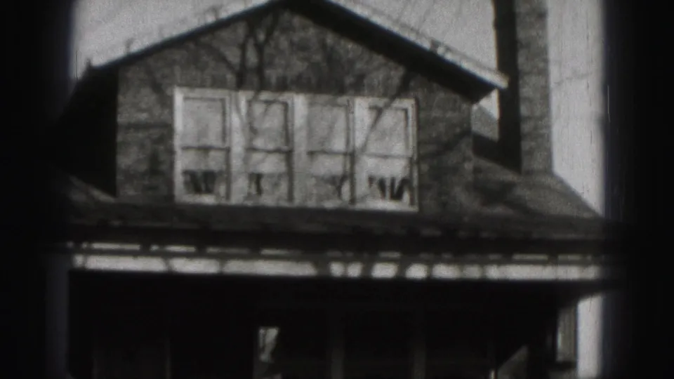 Black-and-white 8mm view of the Harrisburg house facade, with multi-pane windows above a shadowed front porch.