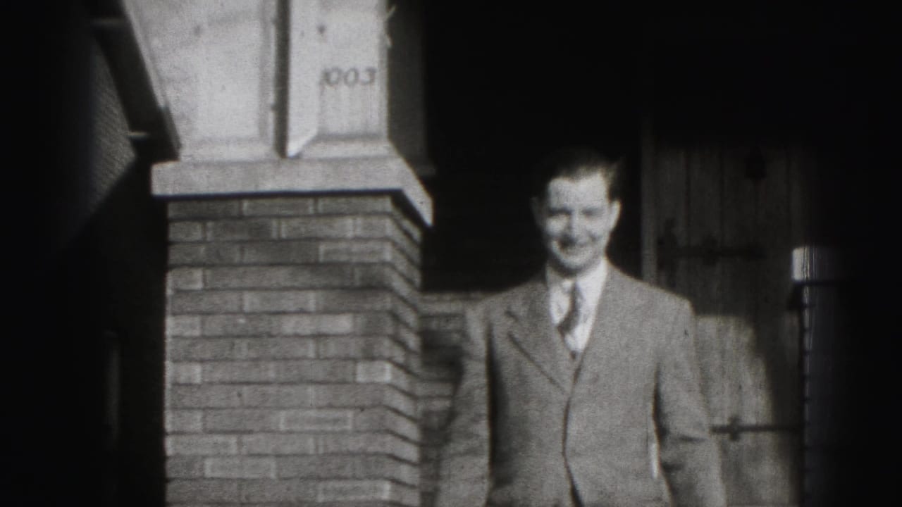 A suited man smiles toward the camera beside a brick residential porch in 1946 Harrisburg home-movie footage.