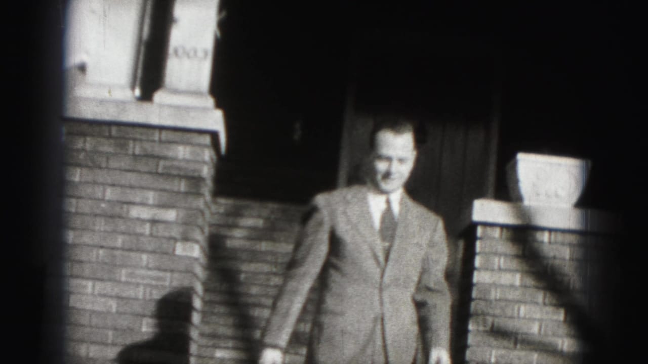 The suited man descends the brick steps of a Harrisburg residence, lit by strong contrast in black-and-white 8mm footage.