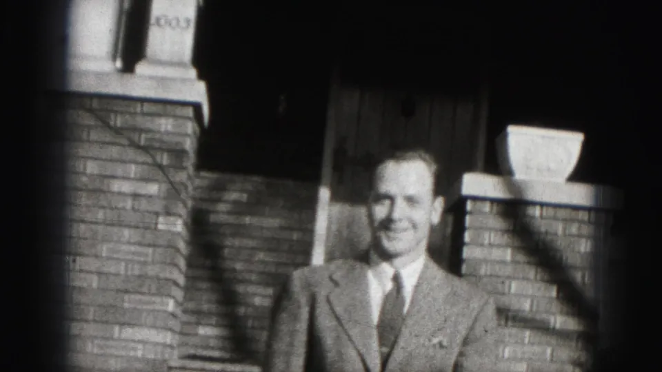 A smiling man in a suit approaches the camera outside the brick-front Harrisburg home.