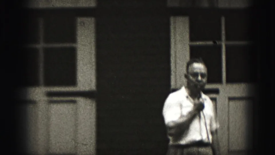 In 1946 New Cumberland footage, a man in a light shirt holds a microphone outside a building with tall multi-pane windows.