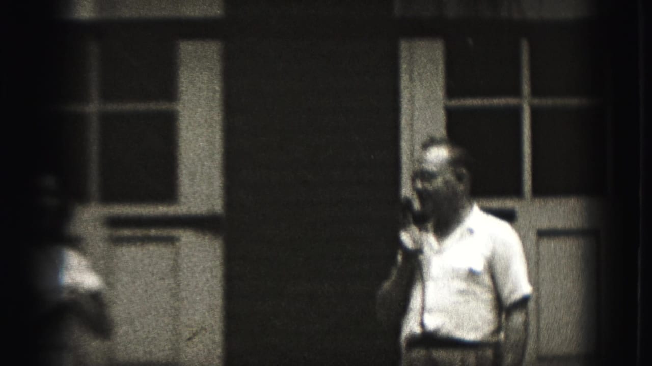 The man continues holding the microphone near the building while a blurred foreground figure partially obscures the 1946 New Cumberland view.