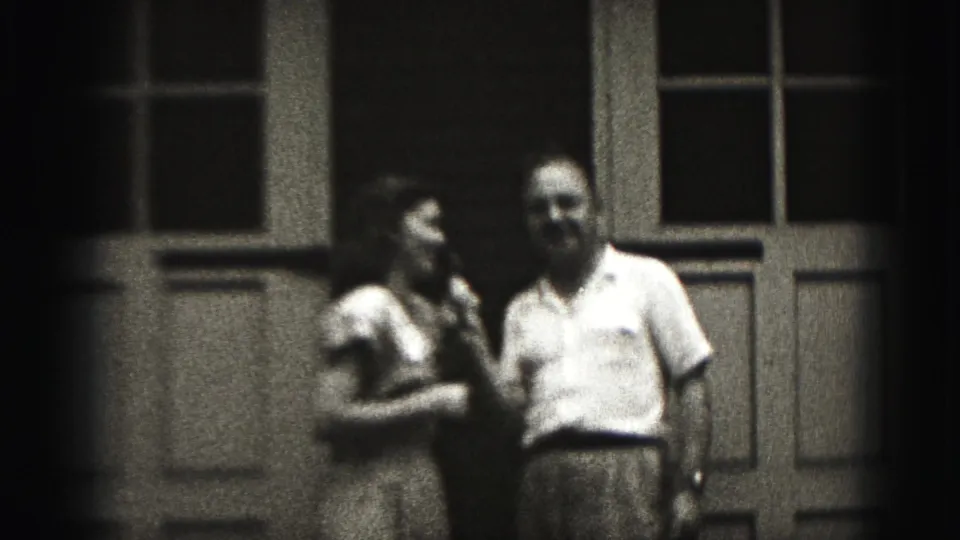 In 1946 New Cumberland home-movie footage, a woman in a light dress stands beside a man in a short-sleeved shirt outside a paneled door.