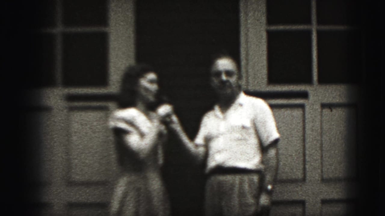 Woman and man stand outside a building sharing a microphone.