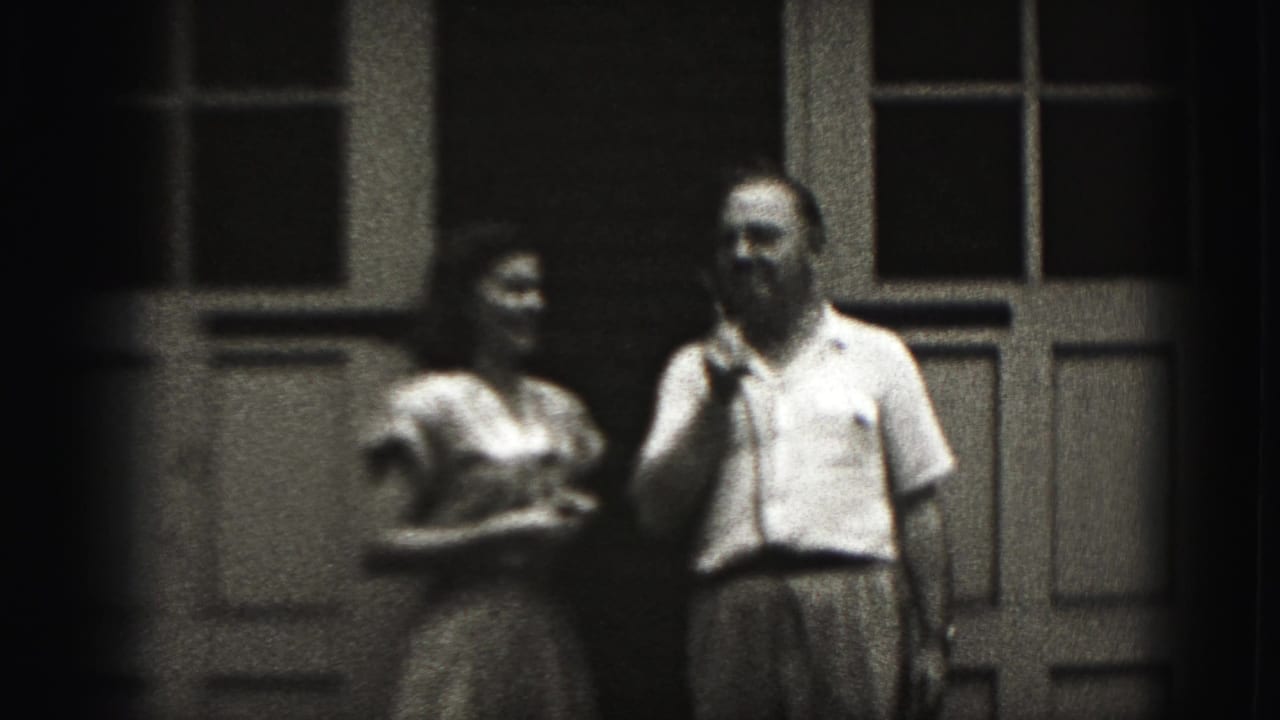 Man holds a telephone receiver beside a woman near a windowed exterior door.