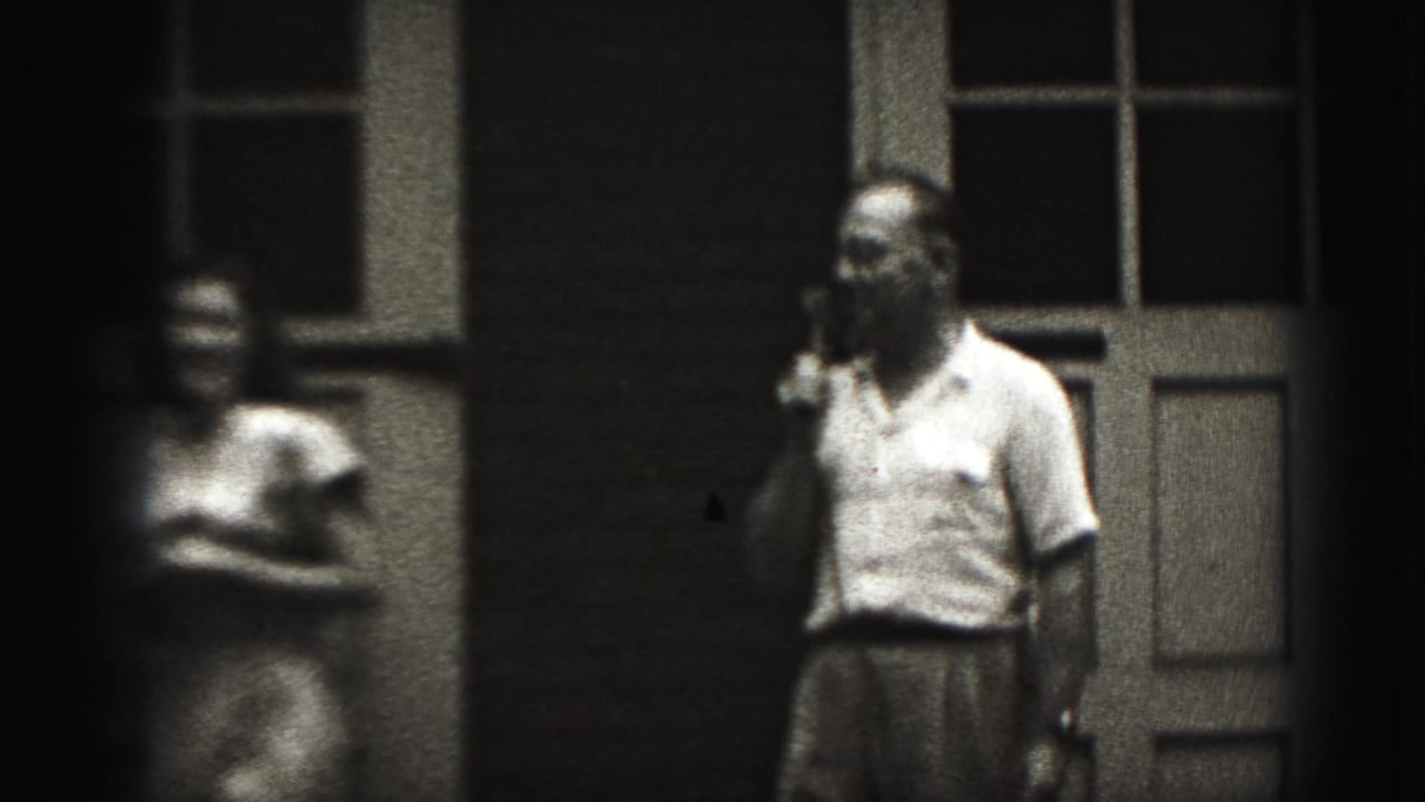 Man keeps a telephone receiver to his ear as a blurred woman stands nearby.